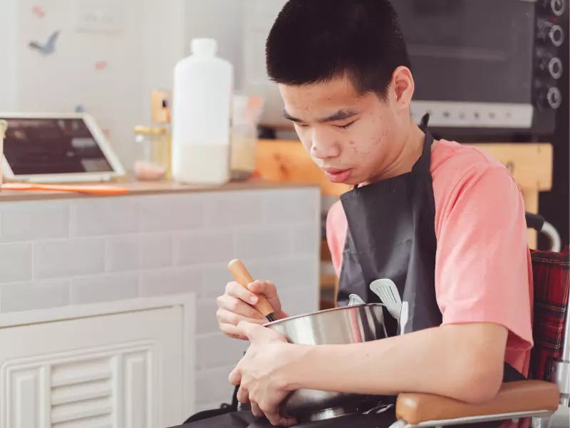 Disabled boy in wheelchair mixing in mixing bowl in kitchen