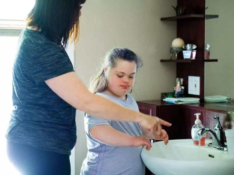 Disabled girl with down syndrome in home with carer washing hands in bathroom sink