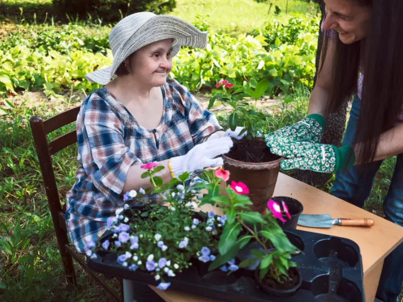 Woman with down syndrome outside potting plants with carer at community garden