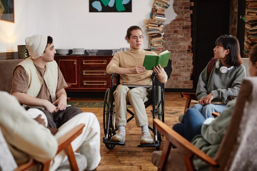 Inclusive, disabled reading group with focus on disabled male in wheelchair reading a book out loud