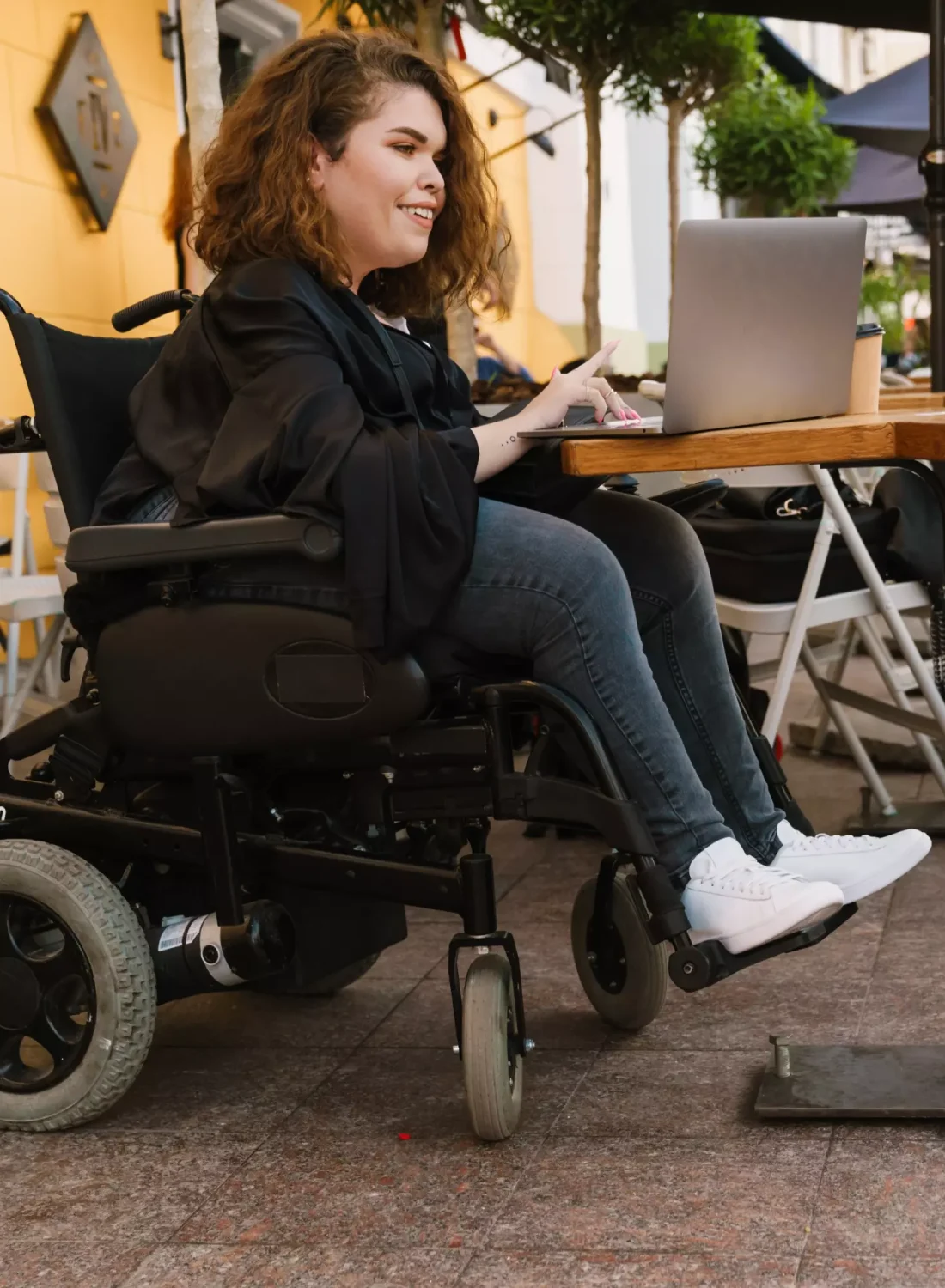 Disabled woman in wheelchair sitting at table at cafe using laptop